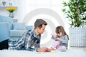 Father and little daughter having quality family time together at home. dad with girl lying on warm floor drawing with colorful