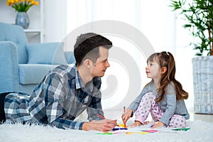 Father and little daughter having quality family time together at home. dad with girl lying on warm floor drawing with colorful