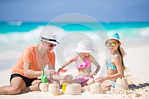 Father and little daughters making sand castle at tropical beach