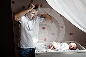 Father and little kid in the nursery. The first year of life. Uncertainty and fear of a child. Daddy does not know what