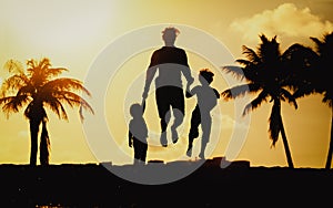 Father with little son and daughter jumping at sunset beach