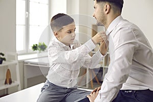 Father and little son dressing up and putting on white shirts for special family occasion