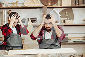 Father and little son with drill perforating wood plank at workshop