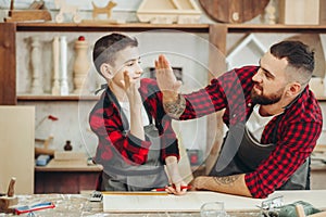 Father and little son giving high five while visiting woodworking masterclass.