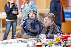 Father and little son having fun on toy exposition, indoors.