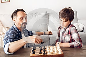 Father and little son at home sitting at table playing chess dad moving piece concentrated