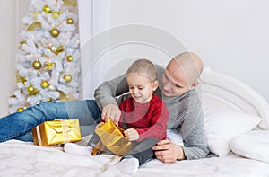 Father and little son lie on bed. They unpack Christmas gifts