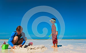 Father and little son play with sand on beach