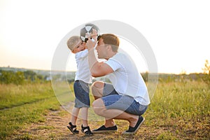 father with a little son plays football on the green grass in the park. Happy family having fun and playing football