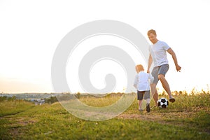 father with a little son plays football on the green grass in the park. Happy family having fun and playing football