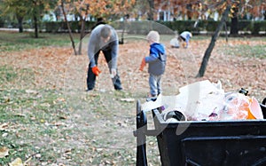 Father and little son scavenging in the park. Background - trash and litter bin. The concept of ecology and protecting the planet