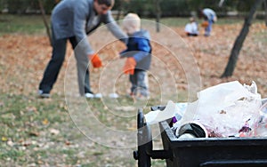 Father and little son scavenging in the park. Background - trash and litter bin. The concept of ecology and protecting the planet