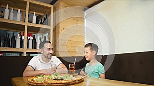 Father and little son sitting in cafe with juice and drinking