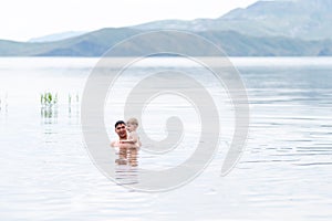 Father with little son swimmind in sea, beautiful landscape sea and mountines photo