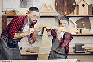 Father and little son testing hand-made wood sward evenness at workshop