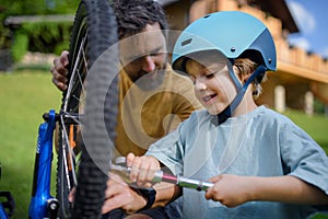 Father with little son together preparing bicycle for a ride, pumping up tyres in garden in front of house.