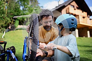 Father with little son together preparing bicycle for a ride, pumping up tyres in garden in front of house.