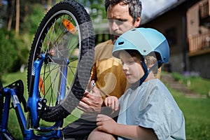 Father with little son together preparing bicycle for a ride, pumping up tyres in garden in front of house.