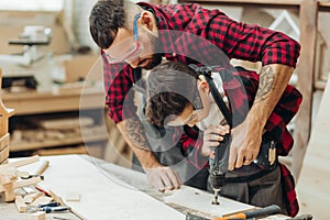 Father and little son working with drill perforating wood plank at workshop