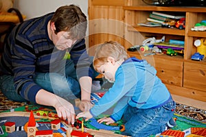 Father and little toddler boy playing with wooden railway, indoors. Happy family, man and cute child moving trains.