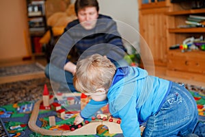 Father and little toddler boy playing with wooden railway, indoors. Happy family, man and cute child moving trains.