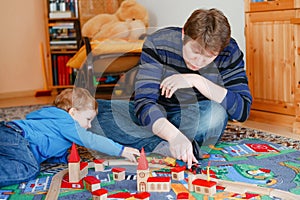 Father and little toddler boy playing with wooden railway, indoors. Happy family, man and cute child moving trains.