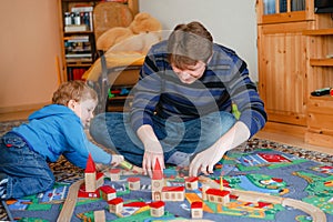 Father and little toddler boy playing with wooden railway, indoors. Happy family, man and cute child moving trains.