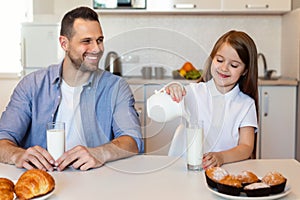 Father Looking At Daughter Pouring Milk In Glass In Kitchen