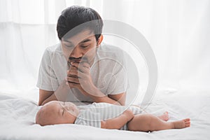 Father looking at his baby son`s face while sleeping on the bed
