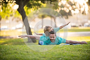 Father lying on grass, with excited happy little child son on shoulder. Carefree two man generations family having fun.