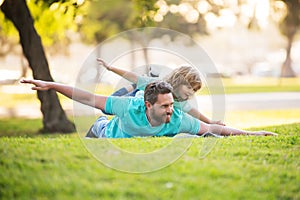 Father lying on grass, with excited happy little child son on shoulder. Carefree two man generations family having fun