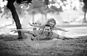 Father lying on grass, with excited happy little child son on shoulder. Carefree two man generations family having fun