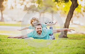 Father lying on grass, with excited happy little child son on shoulder. Carefree two man generations family having fun