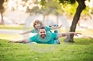 Father lying on grass, with excited happy little child son on shoulder. Carefree two man generations family having fun