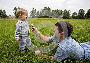 Father lying on his stomach tickles son 1.3 years with sprig .