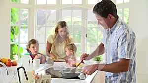 Father Making Scrambled Eggs For Family Breakfast In Kitchen