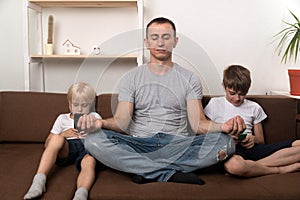 Father meditates while children using gadgets. Dad has calmed his sons and relaxing