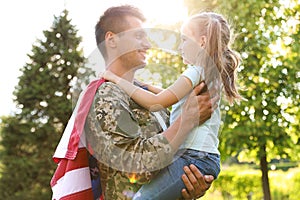 Father in military uniform with American flag holding his daughter at green park