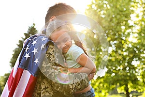 Father in military uniform with American flag holding his little daughter at park