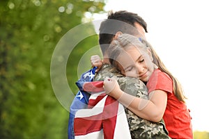 Father in military uniform with American flag hugging his little daughter at park