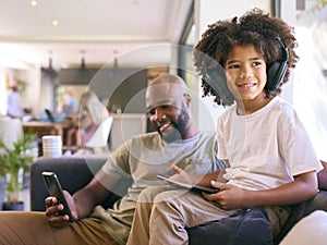 Father With Mobile Phone And Son Using Digital Tablet With Headphones At Home 