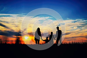 Father, mother, and children hold hands on a sunset background.