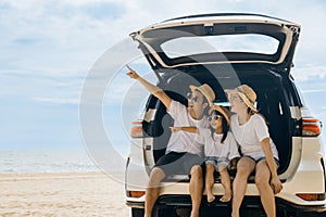 Father, Mother and daughter enjoying road trip sitting on back car and point finger out blue sky