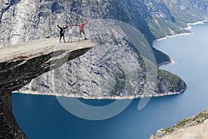 Father, mother and daughter holding and waving hands on Trolltunga rock formation. Jutting cliff is in Odda, Hordaland county,