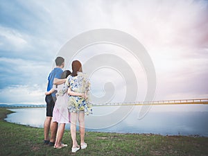 Father, mother and daughter hugging while watching nature and sunset at the lake.Concept of happy family travel