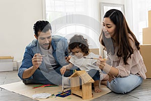 Father Mother and daughter painting coloring with watercolor on the wooden house mock up. Sitting on the floor in living room.