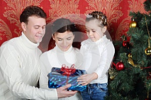 Father, mother and daugther hold gift near Christmas tree