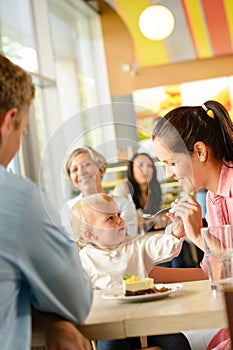 Father and mother feeding child cake cafe