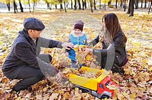 Father, mother and his little son rest in autumn garden. Cute boy playing with the toy car in the autumn park.