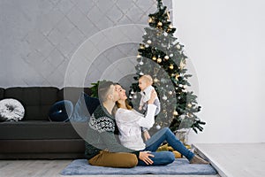 A father and mother hold a young son near a Christmas tree. Christmas decoration of the interior of the house. The concept of a fa